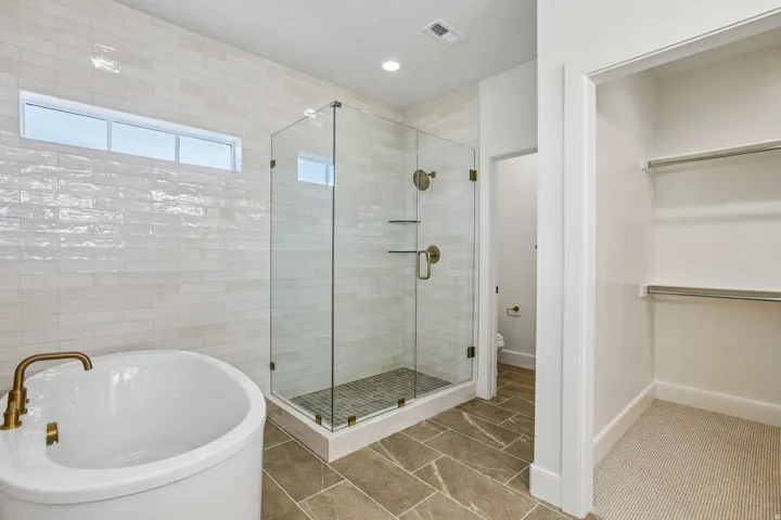 Freestanding tub with brass-finish fixtures, glass-enclosed shower with brass-finish fixtures, and a walk-in closet with built-in shelving
