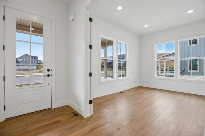 Recessed lighting, wood-finish flooring, white walls, multiple windows, and a glass-paneled entry door