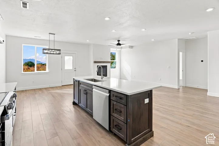 Open-concept layout featuring wood-finish flooring throughout, a large kitchen island with integrated sink, recessed lighting, and a modern ceiling fan
