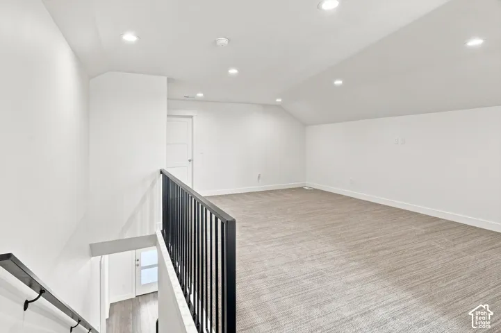 Open concept loft space with recessed lighting, angled ceilings, and neutral carpeting