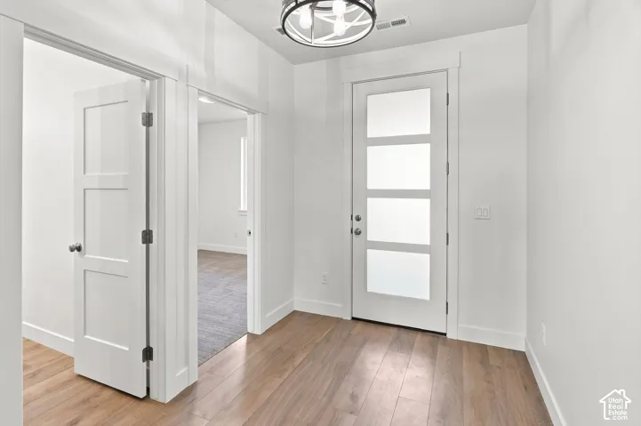 Wood-finish flooring, contemporary ceiling fixture, white paneled doors, and a front entry door with frosted lites