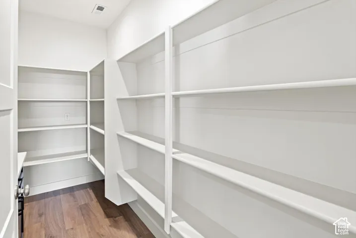 Walk-in pantry featuring extensive built-in white shelving, wood-finish flooring, and a white interior door