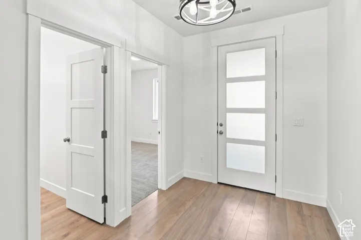 Wood-finish flooring, white walls, modern ceiling light fixture, contemporary entry door with frosted panels, and interior doors with panel details