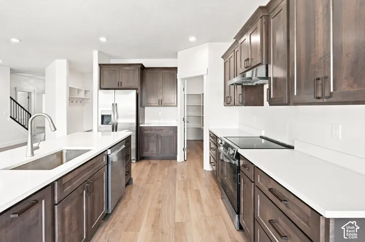 Kitchen featuring stainless steel appliances, wood-finish flooring, dark wood cabinetry, white countertops, and a stainless steel sink with a gooseneck faucet