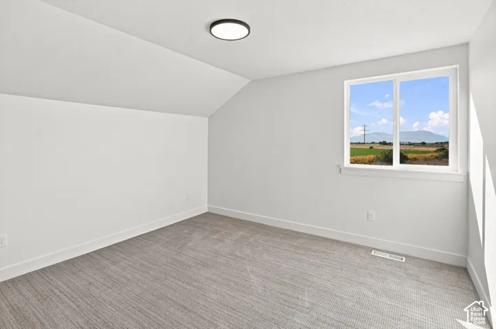 Sloped ceiling with recessed lighting, large window with expansive outdoor scenery, wall-to-wall carpeting, and bright white walls