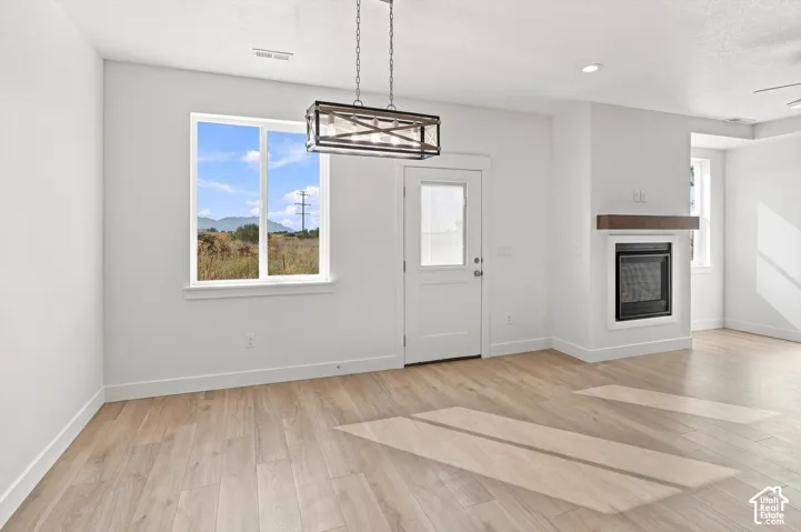 Wood-finish flooring, white walls, built-in fireplace with a wood mantle, recessed lighting, and a modern chandelier