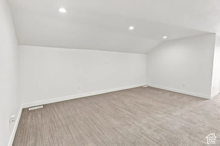 Recessed lighting, sloped ceiling, light-toned carpeting, white walls, and white trim