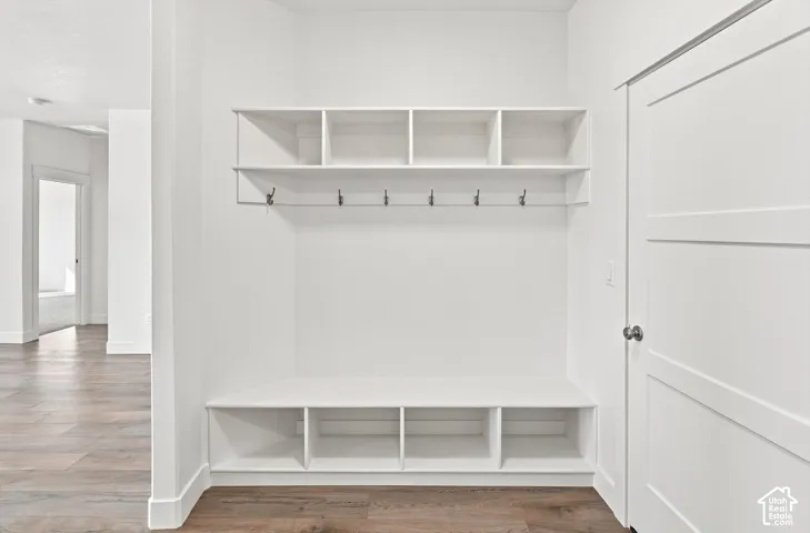Built-in white storage unit featuring open shelving, integrated bench, and wall-mounted hooks