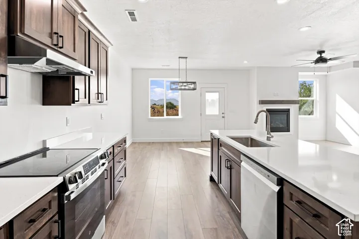 Wood-finish flooring throughout, dark wood-finish cabinetry, white countertops, built-in stainless steel appliances, and a modern ceiling fan