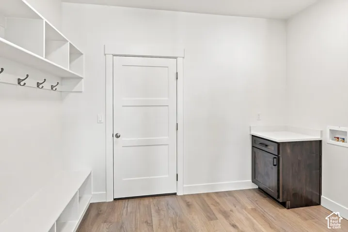 Built-in white cubbies with coat hooks, white bench storage, wood-finish flooring, and a dark wood-finish vanity with a light-toned countertop