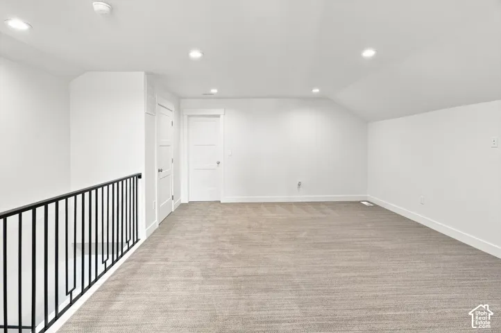 Spacious carpeted area featuring recessed lighting, white walls, and a black metal railing