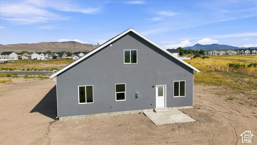 Gray exterior siding with white trim, multiple windows, and a concrete patio