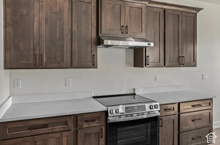 Wood-finish cabinetry with dark hardware, light-toned countertops, and stainless steel range with overhead ventilation