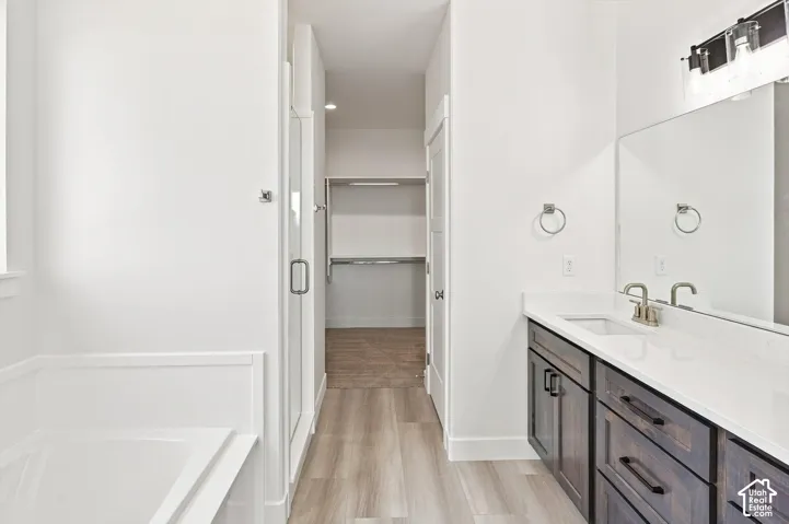 Built-in soaking tub, glass-enclosed shower, wood-finish flooring, dual-sink vanity with stone countertop, and walk-in closet with shelving