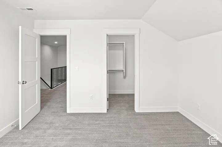 Neutral tone wall paint, light-toned carpeting, white trim, attic-style ceiling, and a built-in closet with shelving