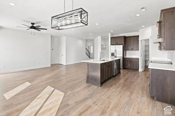 Open-concept living area with wood-finish flooring, a kitchen island, dark wood cabinetry, white countertops, and recessed lighting