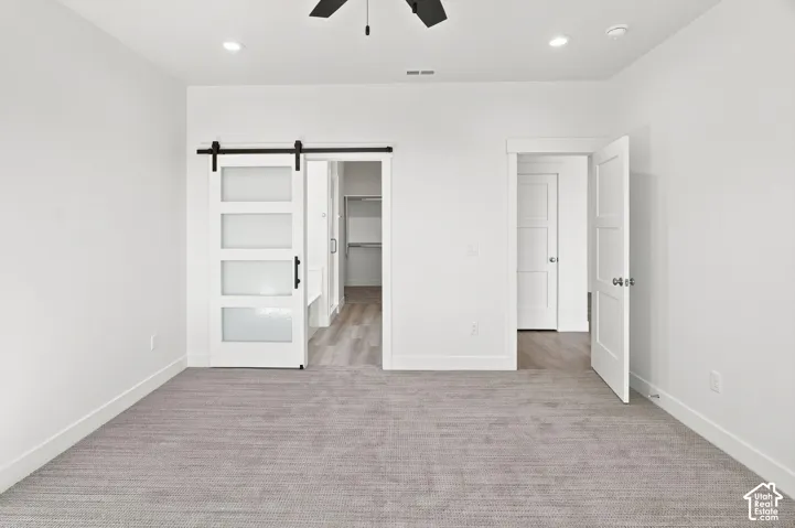 Recessed lighting, ceiling fan, grey carpet flooring, white walls, and a white barn door with frosted glass panels