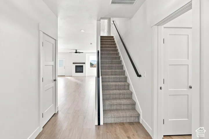 Wood-finish flooring, staircase with carpeted treads and black handrail, modern white interior doors, and recessed lighting