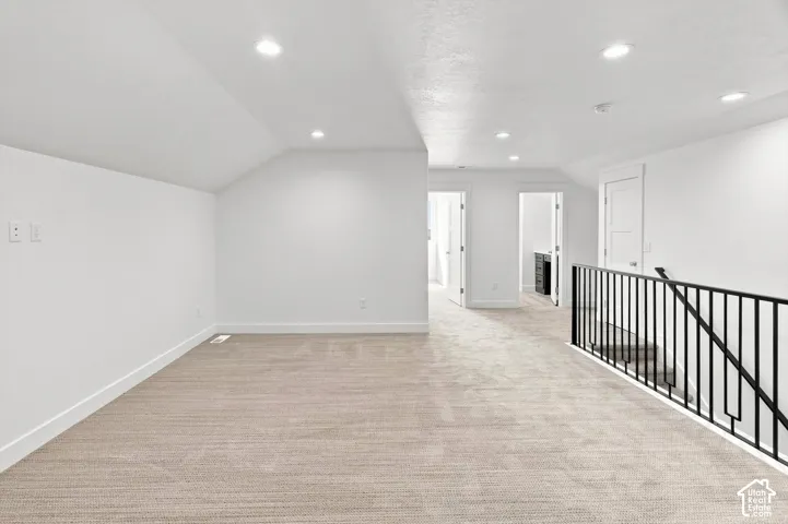 Carpeted loft area with recessed lighting, white walls, and a black metal railing