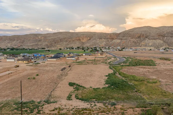 Expansive undeveloped land with a paved road, surrounded by residential properties and natural desert landscaping, set against a mountainous backdrop