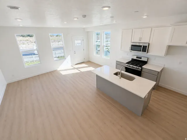 Open-concept living area featuring wood-finish flooring, recessed lighting, a kitchen island with an undermount sink, and stainless steel appliances