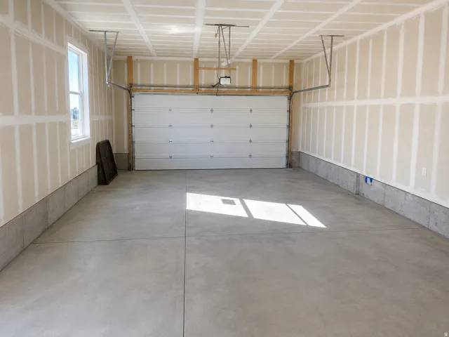 Concrete flooring, single window, overhead garage door, exposed ceiling joists, partially finished walls