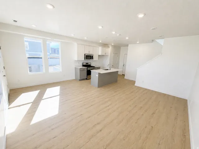 Open concept living area featuring wood-finish flooring, white walls, recessed lighting, and a kitchen with an island, white upper cabinetry, and stainless steel appliances