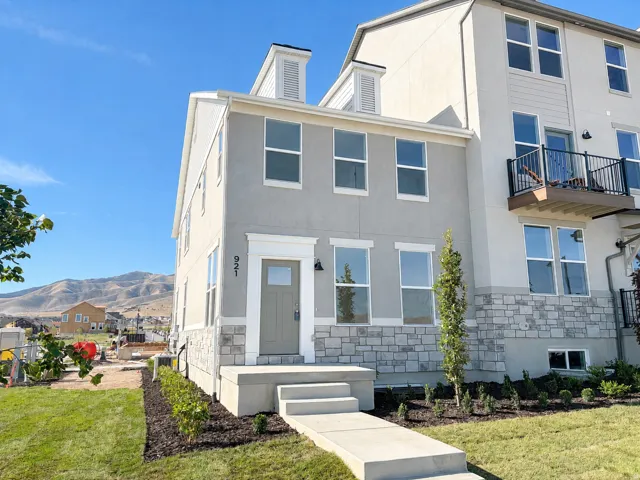 Two-story exterior with stucco and stone accents, featuring a prominent front door with side sconces, multiple large windows, and a concrete pathway leading to the entrance