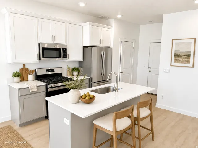 Kitchen featuring recessed lighting, two-tone cabinetry with upper white and lower gray finishes, stainless steel appliances, a center island with an undermount sink, and wood-finish flooring