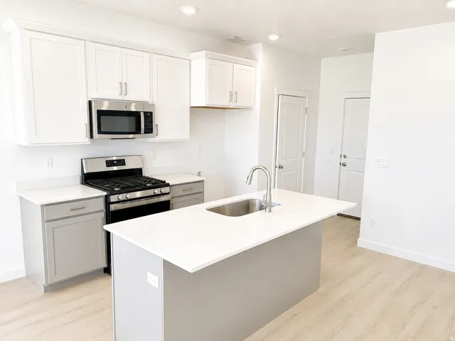 Kitchen featuring an integrated island with a stainless steel sink and gooseneck faucet, light-toned wood-finish flooring, two-tone cabinetry, and stainless steel appliances