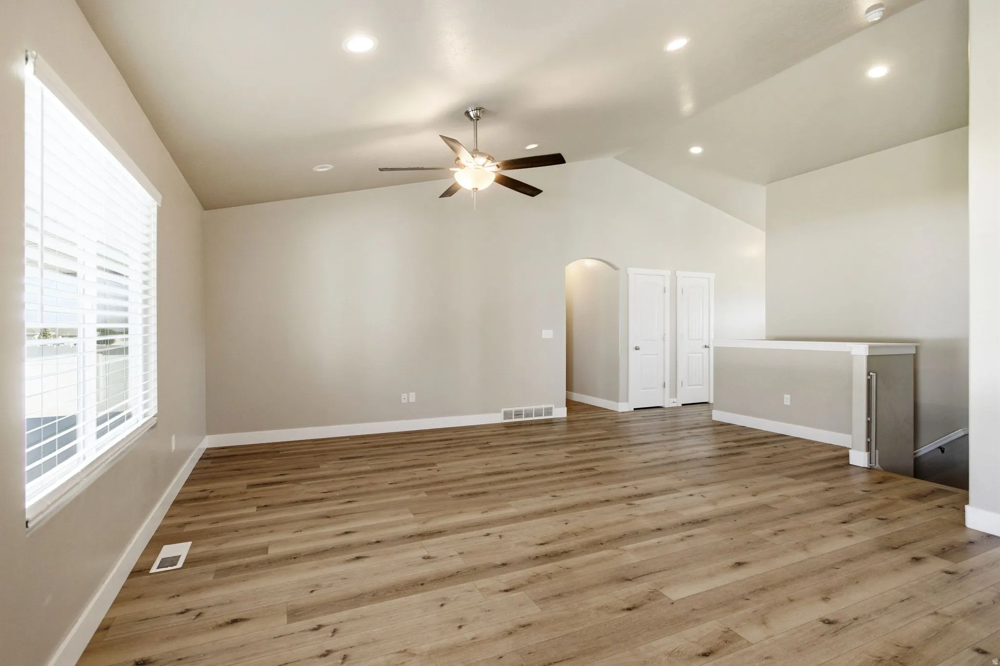 Vaulted ceiling with recessed lighting, wood-finish flooring, ceiling fan with light fixture, large window with blinds, and an arched doorway