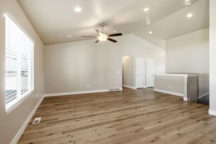 Vaulted ceiling with recessed lighting, wood-finish flooring, ceiling fan with light fixture, large window with blinds, and an arched doorway