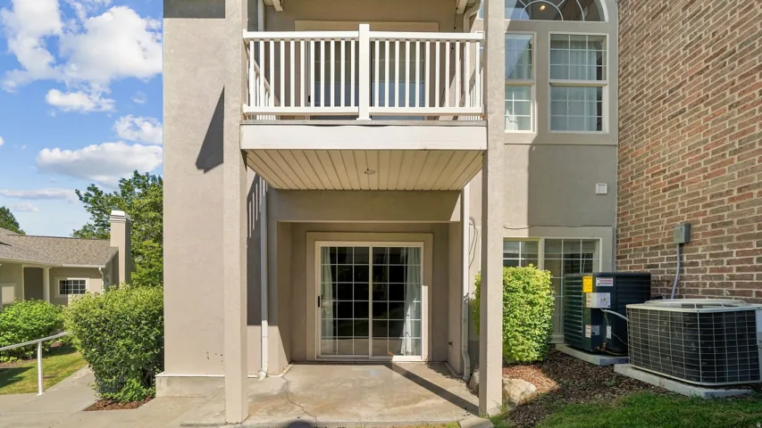 Exterior stucco finish, upper-level balcony with white railings, lower-level sliding glass door, arched window, and brick-clad wall