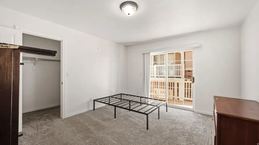 Plush gray carpeting, white painted walls, ceiling-mounted light fixture, sliding glass door with balcony access, and built-in closet shelving