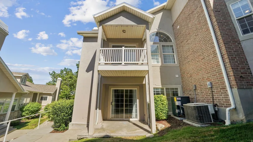 Stucco exterior with brick accent, featuring an upper-level balcony with white railing, and a ground-level patio with sliding glass doors
