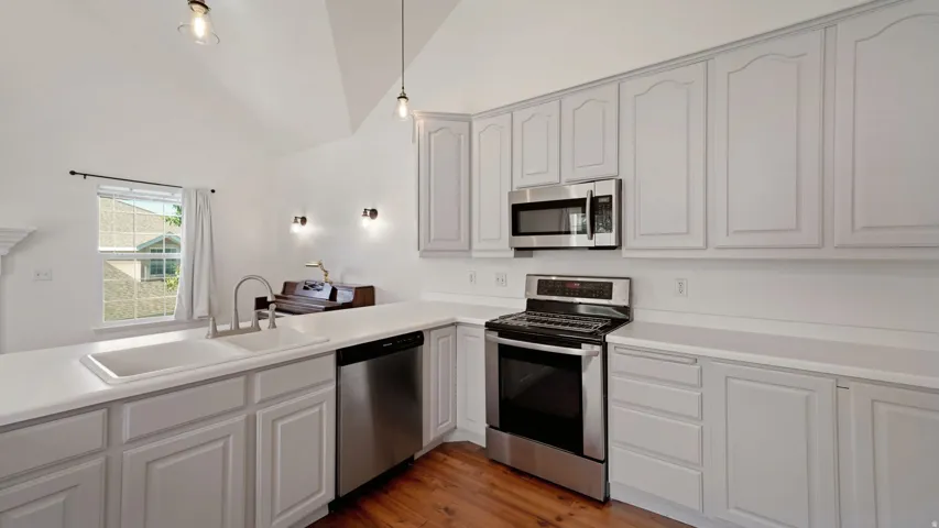 Vaulted ceiling kitchen featuring light cabinetry, stainless steel appliances, a double basin sink, and wood-finish flooring