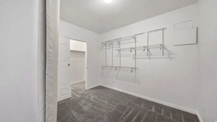 Room featuring gray patterned carpet, white walls, and a built-in wire shelving system