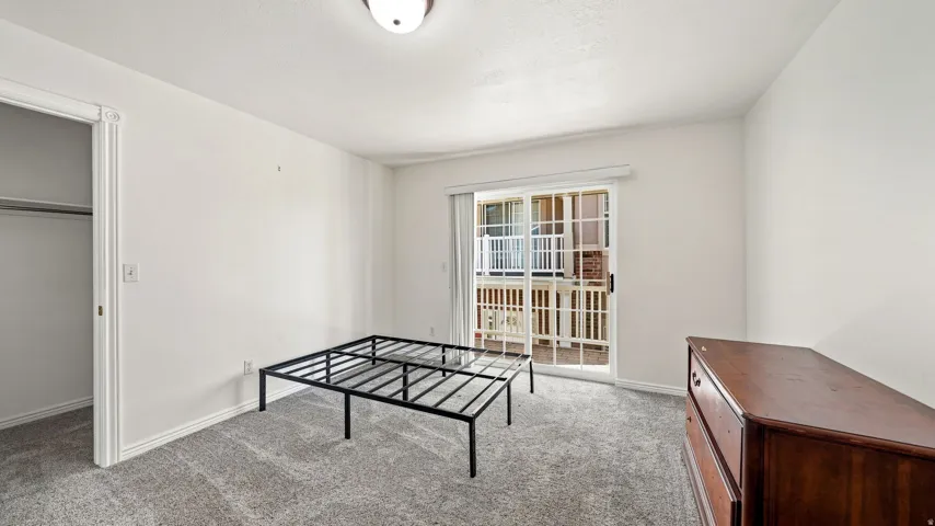 Plush carpet flooring, white painted walls, ceiling-mounted light fixture, sliding glass door with balcony access, and an open closet
