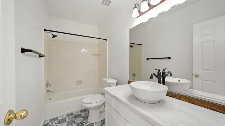 Contemporary bathroom with patterned floor tile, white vanity, vessel sink, and a combination shower/tub with black fixtures