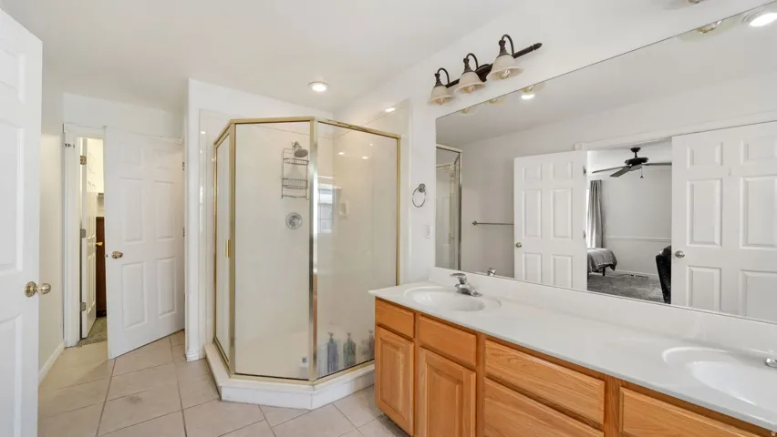 Master bathroom featuring dual vanity with integrated sinks and wood-finish cabinetry, tile flooring, and a glass-enclosed shower with a gold-tone frame
