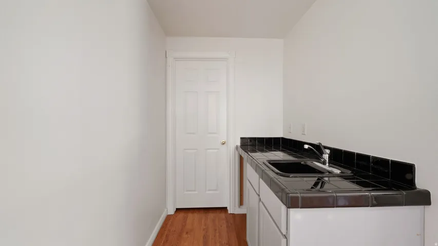 White paneled door, wood-finish flooring, built-in cabinetry, black tile countertop, integrated sink with faucet