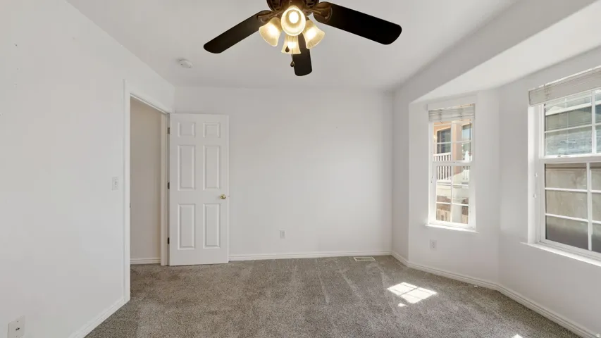 Recessed window alcove with two windows, ceiling fan with integrated lighting, paneled interior door, and gray carpet