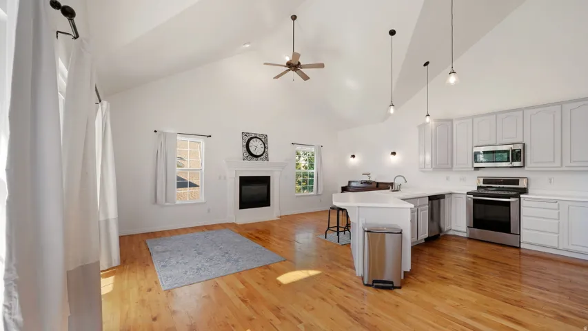 Vaulted ceilings, wood-finish flooring, white kitchen cabinetry, stainless steel appliances, and a fireplace with a mantel