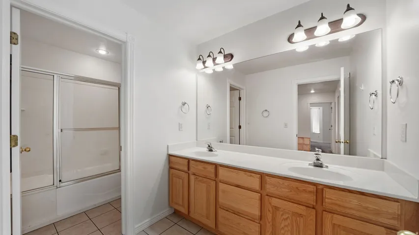Dual vanity with wood-finish cabinetry, white countertops, and integrated sinks