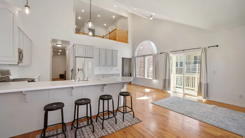 Vaulted ceilings, wood-finish flooring, white cabinetry, a kitchen island with seating, and a large arched window