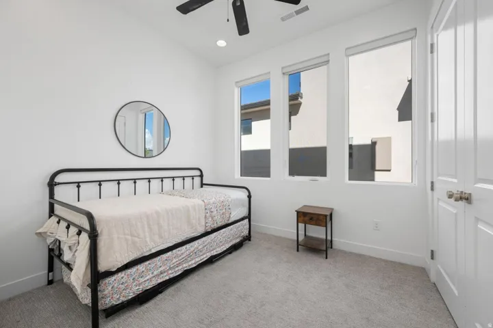 White walls with gray carpeting, three rectangular windows, and a black ceiling fan