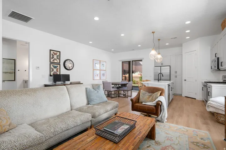 Open-concept living area featuring wood-finish flooring, recessed lighting, and a white kitchen with stainless steel appliances