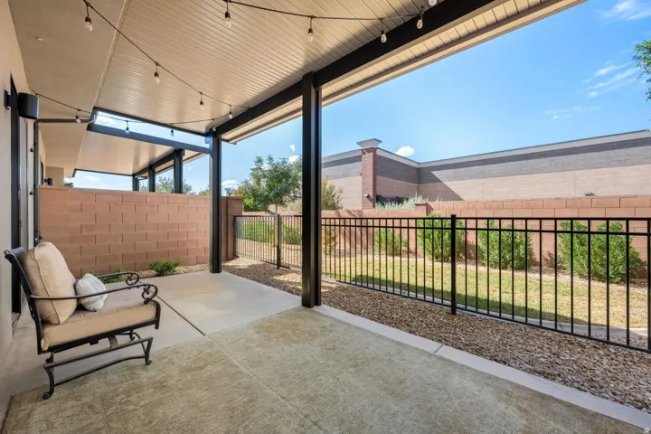 Covered patio area with concrete flooring, string lighting, a block wall, and a black metal fence