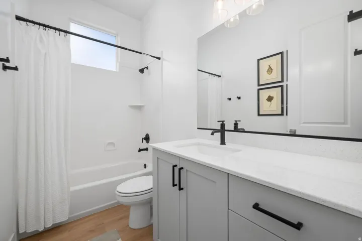 Light wood-finish flooring, a white bathtub with an integrated shower, and an elongated toilet