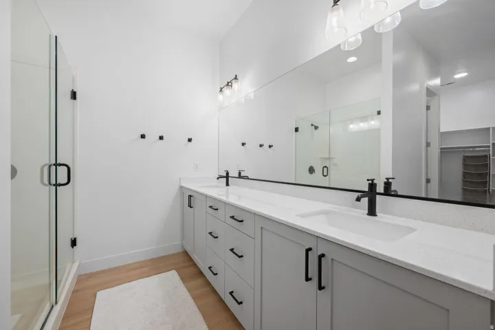 Dual basin vanity with stone-finish countertop, wood-finish flooring, glass-enclosed shower, and built-in closet organization